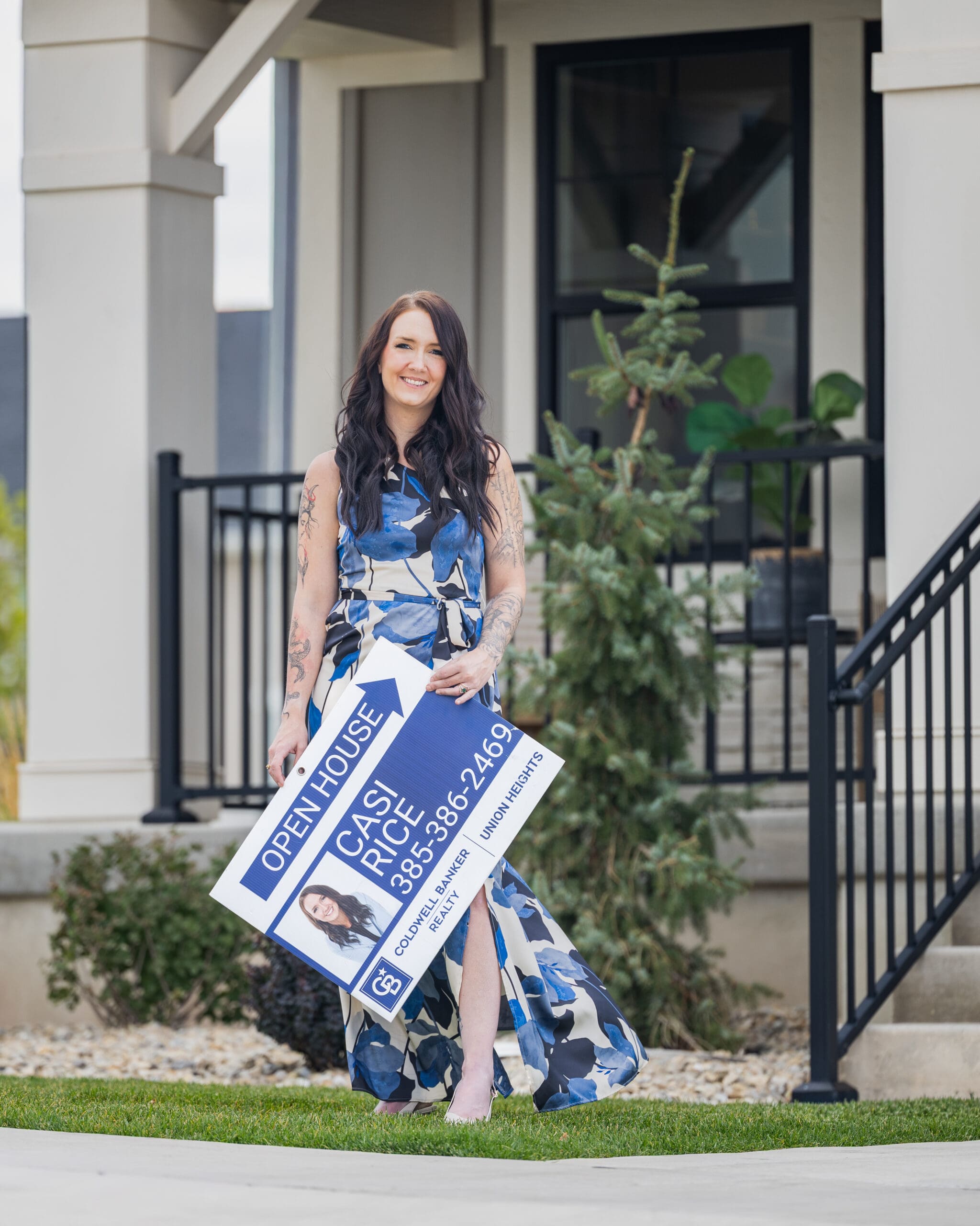 Real estate agent smiling outdoors while holding an open house sign during a lifestyle branding photo session, professional marketing imagery in a residential neighborhood setting in Salt Lake City, Utah.